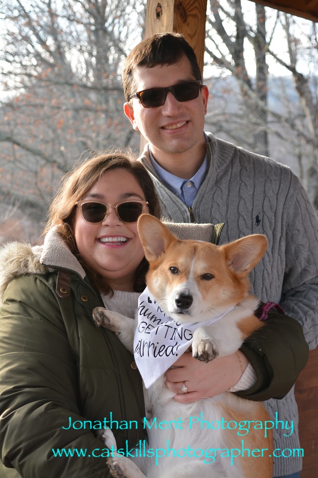 Couple poses with dog. Dog wearing bib that says 'my humans are getting married!'